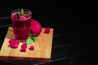 Bir canlı pembe pancar yüzlü siyah bir zemin üzerine uzun bir bardak. Tatlı sebze kokteyl kamış çifti. Taze pancar kesme masa üzerinde küçük küpler kesti. Kopya alanı.