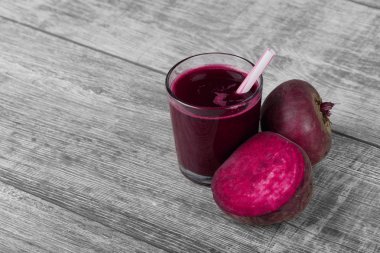 Renkli pancar bir cam ahşap masa arka plan üzerinde küçük bir saman ile harmanlanmış. Bir içki yanında parlak kırmızı pancar yarısı. Besleyici tarım malzemeleri. Kopya alanı.