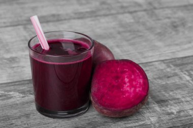 Pancar içecek bir bardak gri bir ahşap zemin üzerinde çizgili bir saman ile yenileniyor. Pembe kırmızı pancar yarısında dilimlenmiş ve bir bütün pancar. Salata için geleneksel malzemeler. Kopya alanı.