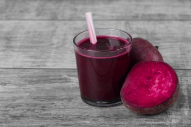 Pancar içecek bir bardak gri bir ahşap zemin üzerinde çizgili bir saman ile yenileniyor. Pembe kırmızı pancar yarısında dilimlenmiş ve bir bütün pancar. Salata için geleneksel malzemeler. Kopya alanı.