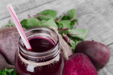 Büyük bir şişe ile bir saman ve soyulmuş pancar sulu bir doku ile bir harika, kırmızı pancar suyu yakın çekim bir resim. Sebze ve yeşillik gri bir ahşap zemin üzerinde. Vejetaryen kokteyller.