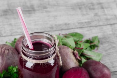 Büyük bir şişe ile bir saman ve soyulmuş pancar sulu bir doku ile bir harika, kırmızı pancar suyu yakın çekim bir resim. Sebze ve yeşillik gri bir ahşap zemin üzerinde. Vejetaryen kokteyller.