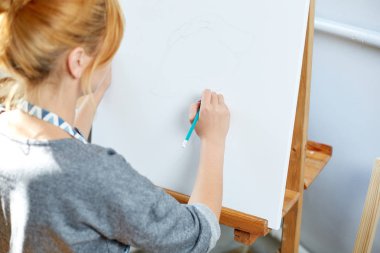 Genç kız boyalar ile petrol renkleri kendi atölyesinde tuval üzerine gülümseyerek. Pencere arka planda. Sanat kavramı.