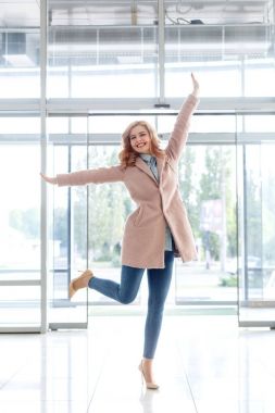 Güzel sarışın genç kız güzel bej bir palto, kot pantolon ve yüksek topuklu.