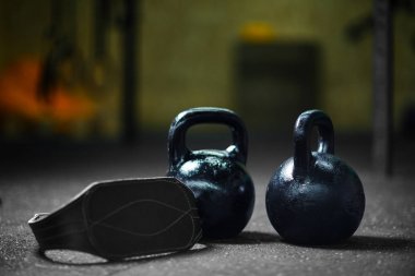 Karanlık bir arka plan bulanık üzerinde gri bir atletik kemer ile iki çelik siyah kettlebells closeup