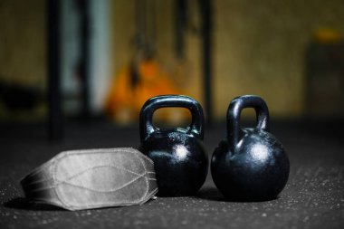 Karanlık bir arka plan bulanık üzerinde gri bir atletik kemer ile iki çelik siyah kettlebells closeup