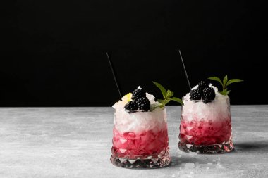 İki bardak kırmızı, pembe meyve suyu, içecekler ve küçük dilimleri buz gri bir tabloya, nane, saman içme bir siyah arka plan üzerine siyah taze yeşil yaprakları. Yaz tatlı içecekler.