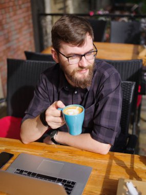 Bir genç sakallı adam onun laptop kullanarak bir kafede oturuyor.