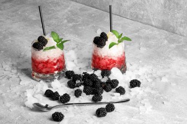 Özlü böğürtlen gri bir tabloya, bir ışık gri arka plan üzerinde kırmızı taze meyve suyu buz ve payet, sarı limon içme siyah taşlarla iki bardak kabuğu. Serinletici içecekler.