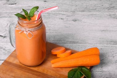 Serinletici bir içki çiğ Havuç soyulmuş tüpler kesme masanın yanında. Bir mason kavanoza Detoks içecek dolu. Bir serin havuç yüzlü dekoratif fesleğen ile gri bir ahşap arka plan üzerinde bırakır.