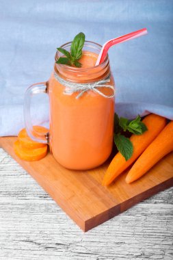 Bir mason kavanoza bir sağlıklı Detoks içecek tam bir yakın çekim resim. Mavi kumaş arka plan üzerinde serinletici bir havuç yüzlü. Vitamin içeceği yanındaki bir kesim masası ve ahşap masa üzerine olgun havuç boruları.