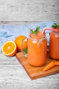 Bulanık havuç kokteyl bir gri üzerine ahşap arka plan yenileme ile parlak portakal, havuç ve iki mason ile gri bir ahşap masa kavanozlar.