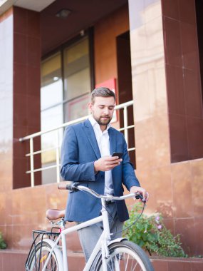 Bir bisiklet, manifatura şehir arka plan üzerinde bir cep telefonu üzerinde sakallı adam. Meşgul hayat kavramı. Kopya alanı.