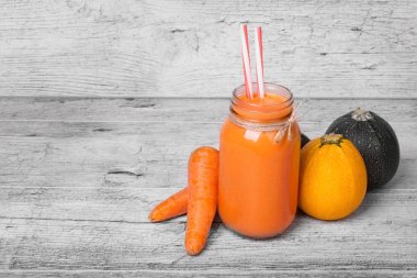 Bir close-up bir mason kavanoza havuçlu yoğurt ve gri bir ahşap zemin üzerinde doğal maddeler. Renkli taze sebze grubunun yanındaki parlak turuncu içecek. Uzay kopyalayın. Sağlık kavramı.