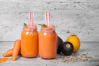 Büyük mason kavanoz havuç yüzlü üzerinde gri bir ahşap arka plan ile. Birkaç havuç tüpler ve kabaklari güzel Cam Kavanoz sebze bardak tam vardır. Vitamini kokteyller. Kopya alanı.