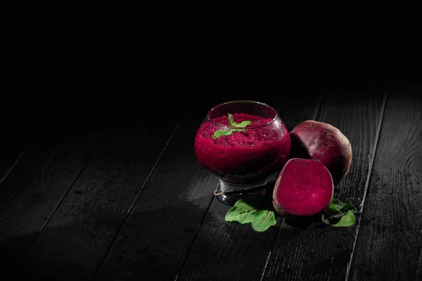 A spacious glass full of dark purple beetroot cocktail on a black table background. Nutritious beets for a healthful vegetarian salad. Vegetable juices for gourmets. Copy space.