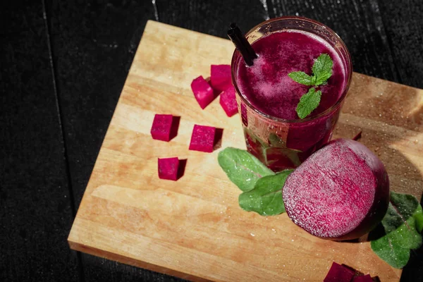 Dan yukarıda kırmızı ile dekoratif baharat ve payet, sulu, kokteyl ile bir bardak güzel bir dizi yarım kırmızı pancar, pancar küpleri ve salata yaprakları siyah bir arka plan kesme masasında dilimlenmiş görüntüleyin.