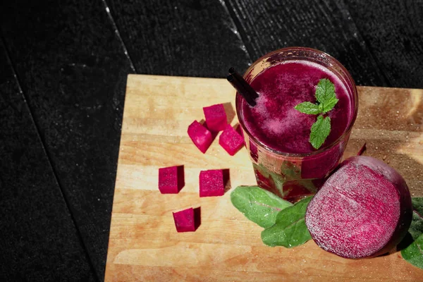 Dan yukarıda kırmızı ile dekoratif baharat ve payet, sulu, kokteyl ile bir bardak güzel bir dizi yarım kırmızı pancar, pancar küpleri ve salata yaprakları siyah bir arka plan kesme masasında dilimlenmiş görüntüleyin.