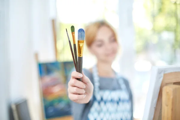 Mladá usmívající se dívka barvy na plátně s olejovými barvami ve vlastní dílně. Okno na pozadí. Koncepce umění. — Stock fotografie