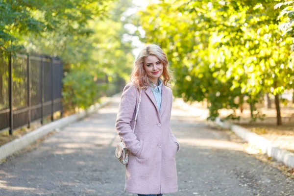 Portret van een jong mooi meisje in een roze jas. In het park. — Stockfoto