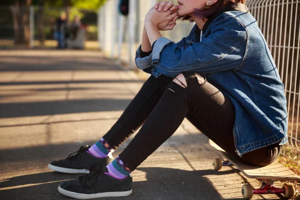 Bir kız parkta bir kaykay üzerinde oturuyor.