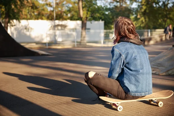 Uma menina está sentada em um skate no parque . — Fotografia de Stock