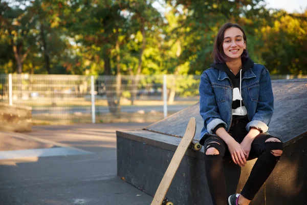 Hermosa joven se sienta al aire libre con un monopatín . — Foto de Stock