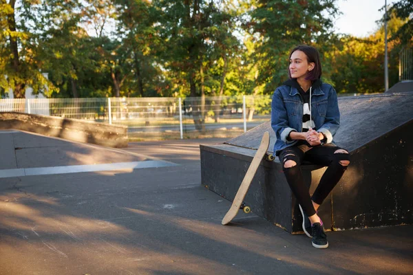 Hermosa joven se sienta al aire libre con un monopatín . — Foto de Stock