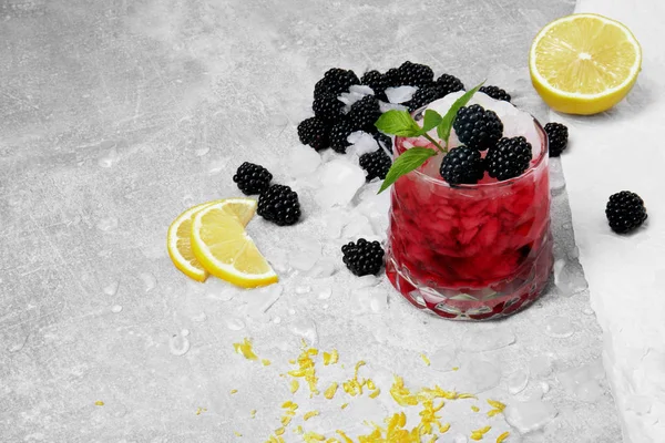 Bir kokteyl buz parçaları, limon, canlı limon, limon kabuğu, özlü böğürtlen sarı parlak dilimleri ile bir bardak meyve suyu ve yeşil nane hafif bir gri arka plan üzerinde bırakır.