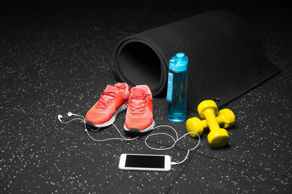 Parlak pembe spor ayakkabı, sarı dambıl, mavi sportif şişe ve siyah pilates mat siyah bir zemin üzerine yakın çekim bir resim. Sportif aksesuarlar renkli bir bileşimi. Sağlıklı yaşam tarzı.