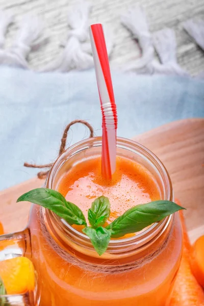 Taze havuç close-up, Portakallı gazoz sulu yeşil ile yenileme ile bir mason kavanoza nane yaprakları ve saman bir ışık arka plan bulanık üzerinde içme çizgili.