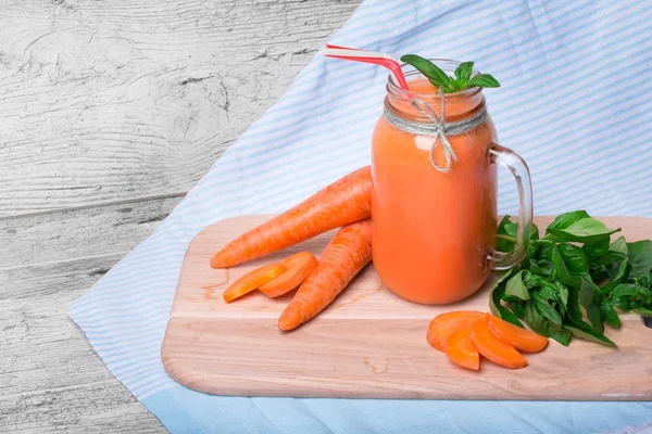 Mavi kumaş arka plan üzerinde serinletici bir havuç yüzlü yakın çekim resim. Bir mason kavanoza bir detoks içecek dolu. Olgun havuç ve yeşil fesleğen yaprakları kesme masanın yanında bir vitamin içeceği.