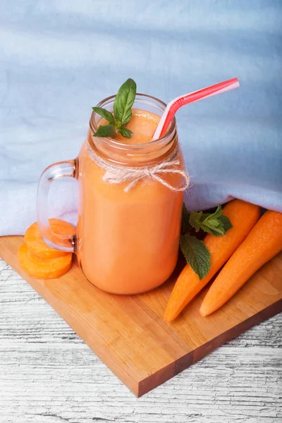 Bir mason kavanoza bir sağlıklı Detoks içecek tam bir yakın çekim resim. Mavi kumaş arka plan üzerinde serinletici bir havuç yüzlü. Vitamin içeceği yanındaki bir kesim masası ve ahşap masa üzerine olgun havuç boruları.