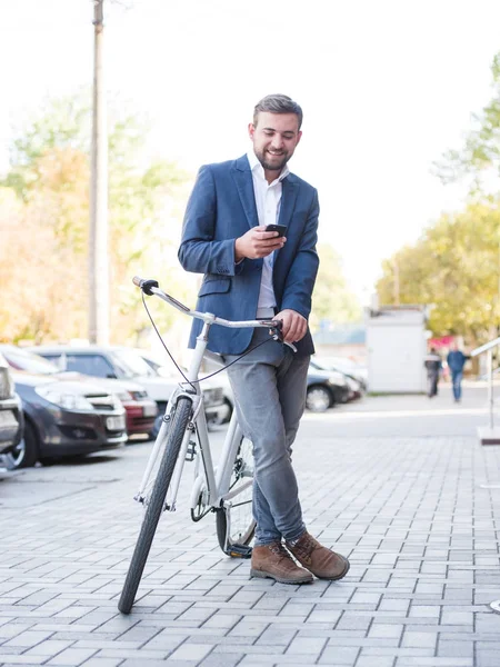 Brodaty mężczyzna z rowerem, wiadomości tekstowe na telefon na tle miasta. Koncepcja zajęty życia. Miejsce. — Zdjęcie stockowe