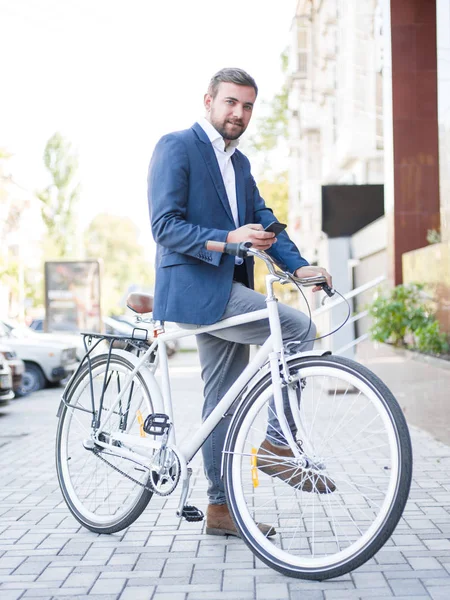 Hombre barbudo con una bicicleta, mensajes de texto en un teléfono en un fondo de la ciudad. Concepto de vida ocupada. Copiar espacio . — Foto de Stock