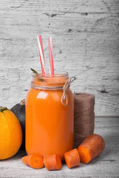 Havuçlu yoğurt, doğal sebze ve gri bir ahşap arka plan iş parçacığında bir bobin bir mason kavanoza bir yakın çekim resim. Yanında birkaç renkli kabakları ve kesilmiş havuç turuncu içecek.