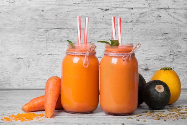 Büyük mason kavanoz havuç yüzlü üzerinde gri bir ahşap arka plan ile. Birkaç havuç tüpler ve kabaklari güzel Cam Kavanoz sebze bardak tam vardır. Vitamini kokteyller. Kopya alanı.