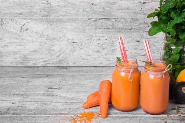 Mason kavanoza gri ahşap masa arka plan üzerinde sağlıklı havuç içecek dolu. 