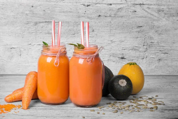 Büyük mason kavanoz havuç yüzlü üzerinde gri bir ahşap arka plan ile. Birkaç havuç tüpler ve kabaklari güzel cam kavanozlarda sebze bardak tam vardır. Vitamini kokteyller. Kopya alanı.