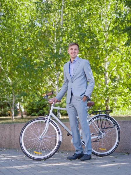 Un tipo con su bicicleta blanca está caminando por la calle contra el telón de fondo de árboles verdes — Foto de Stock