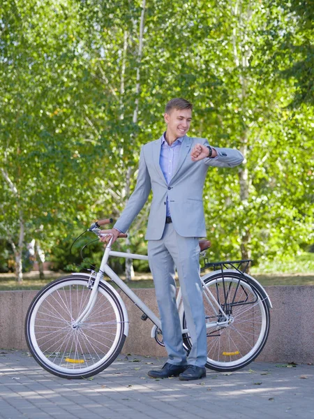 Bir adam onun beyaz bisiklet ile yeşil ağaçlar fon karşı cadde boyunca yürüyor