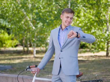 Bir adam onun beyaz bisiklet ile yeşil ağaçlar fon karşı cadde boyunca yürüyor