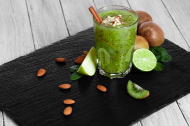 Kalın, kivi milkshake sulu limes ile harmanlanmış ve siyah bir tepsi üzerinde elma kesti. Baharatlar ve ahşap masa arka plan üzerinde fındık ile taze bir alkolsüz içecek. Doğal kompozisyon.