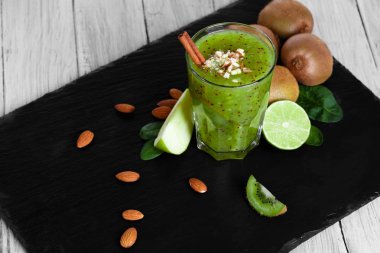 Kalın, kivi milkshake sulu limes ile harmanlanmış ve siyah bir tepsi üzerinde elma kesti. Baharatlar ve ahşap masa arka plan üzerinde fındık ile taze bir alkolsüz içecek. Doğal kompozisyon.