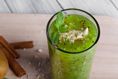 Bir bardak güzel açık yeşil, aromatik nane ile sağlıklı güler yüzlü, baharatlı tarçın ve küçük fındık hafif Resepsiyon arka plan üzerinde yakın çekim resmin. Kivi ve tarçın sopa sonraki bir karışıma kahverengi.