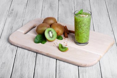 Kivi meyve besleyici vitaminler, tarçın ve ceviz ahşap bir masa ve bir gri tablosudur arka plan dolu. Bir bardağın dolu güler yüzlü sulu kivi, rendelenmiş fındık ve nane bir kesme tahtası üzerinde.