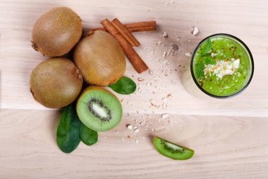 Yukarıdan bir görünümü üzerinde tam ve yarım kivi meyve dekoratif nane yaprakları ve tarçın baharat ile kesim yığını. Ahşap masa lambası arka plan üzerinde krem, kalın kivi smoothie.