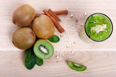 Yukarıdan bir görünümü üzerinde tam ve yarım kivi meyve dekoratif nane yaprakları ve tarçın baharat ile kesim yığını. Ahşap masa lambası arka plan üzerinde krem, kalın kivi smoothie.