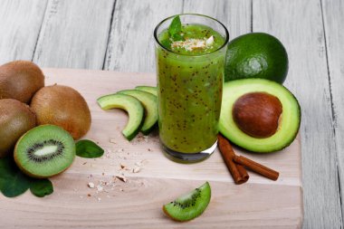 Harika bir kompozisyon bir ışık kesme masasında vejetaryen ürünlerin. Yeşil avokado, kivi bir gri tablosudur arka plan üzerine dilimlenmiş. Besleyici, sağlıklı kivi suyu aromatik nane ve tarçın ile.