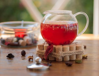 Dekoratif bir stand ışık kırmızı çay ile bir bardak su ısıtıcısı. Geleneksel çay ve kuru kırmızı meyveler ile doğal arka plan bulanık bir kafeterya masada üzerinde ayakta bırakır. Sağlıklı Ürünler kavramı.